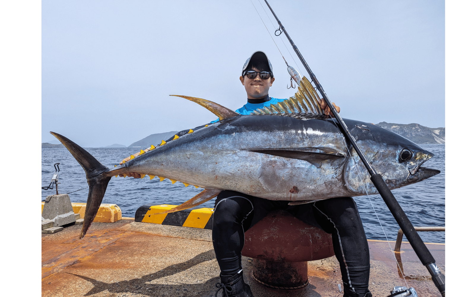Person in wetsuit holding a large fish on a dock with water and sky in the background , fishing rod tailwalk okinawa manbika